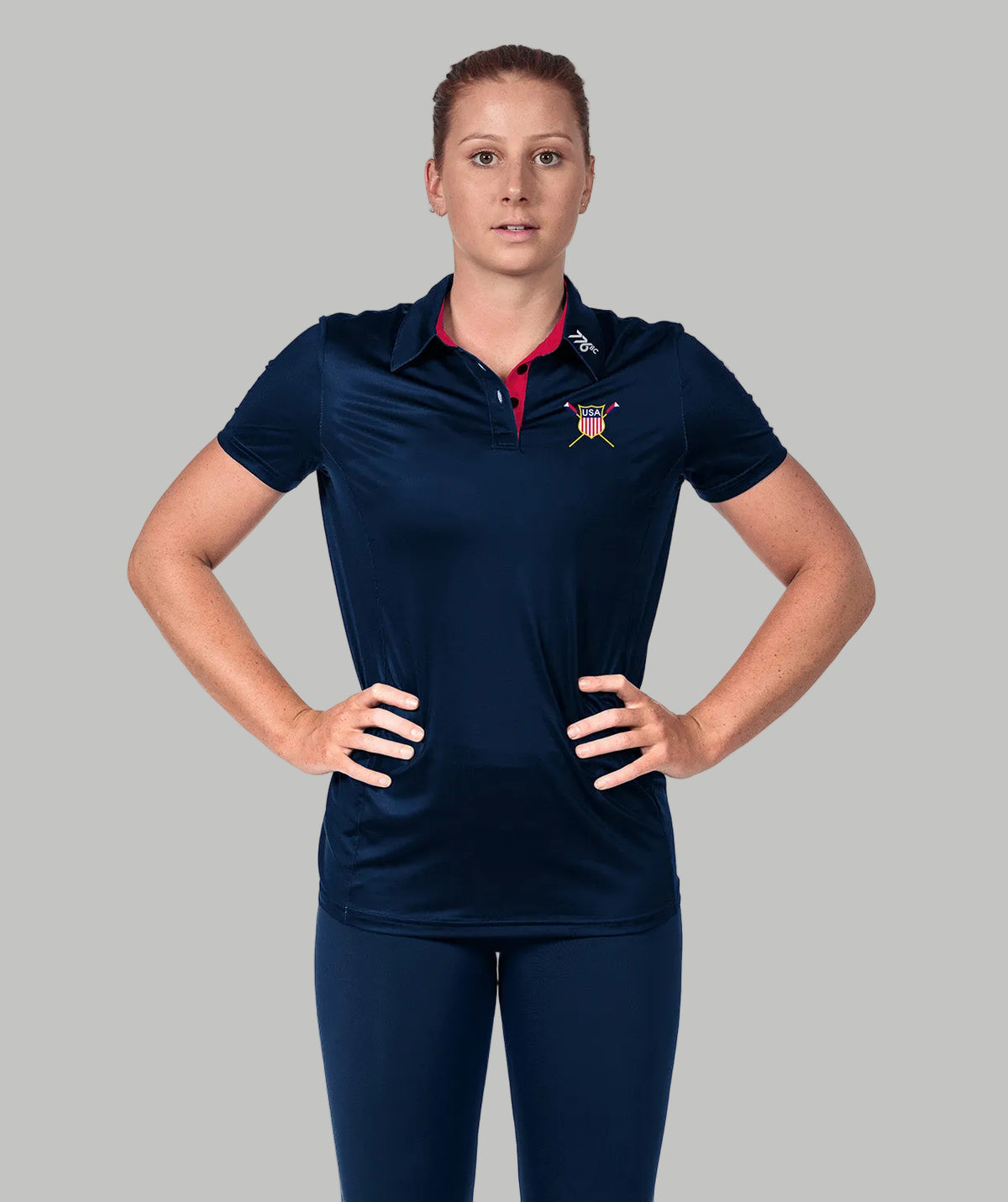 A woman wearing a navy USRowing supporter club polo with the national team crest on the chest.